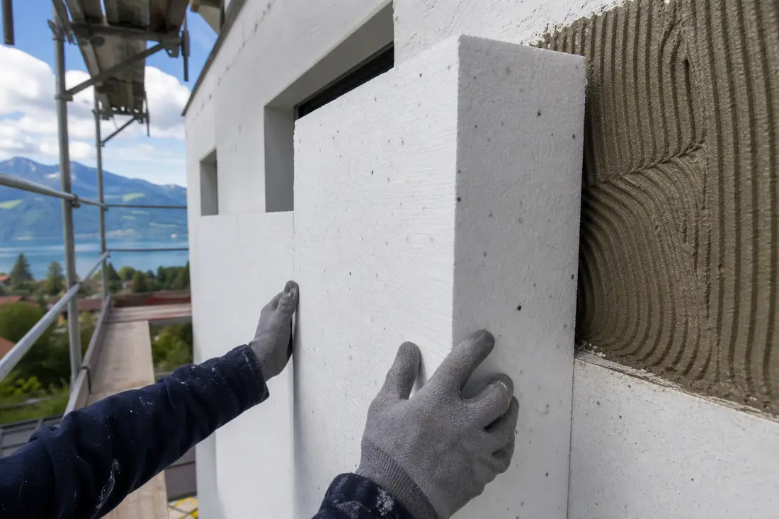Handwerker montiert Dämmplatten eines Wärmedämmverbundsystems an einer Hausfassade in der Deutschschweiz